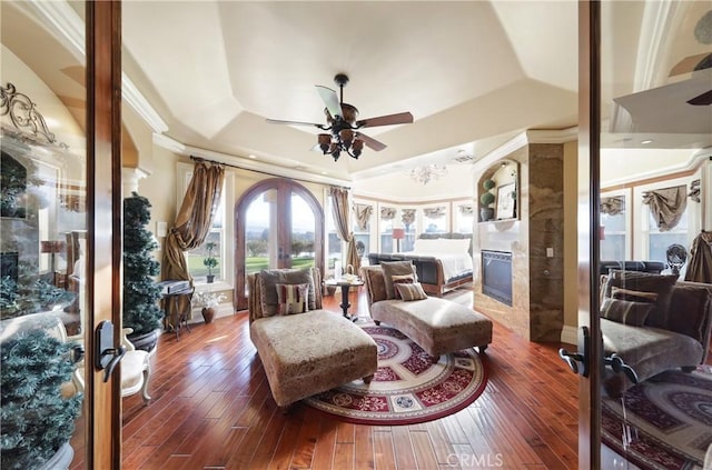 living room with ceiling fan, a tiled fireplace, a raised ceiling, dark wood-type flooring, and french doors