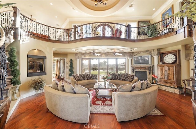 living room featuring ceiling fan, a fireplace, a towering ceiling, and hardwood / wood-style flooring