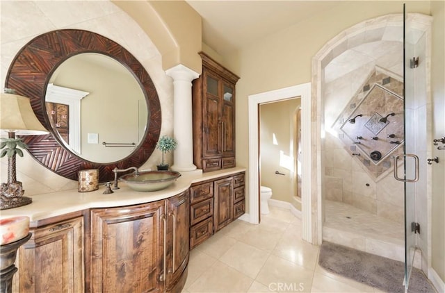 bathroom with toilet, vanity, tile patterned floors, a shower with shower door, and ornate columns