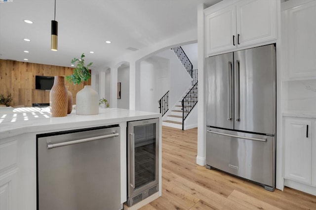 kitchen featuring white cabinetry, light wood-type flooring, appliances with stainless steel finishes, pendant lighting, and beverage cooler