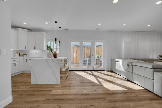 kitchen with a kitchen bar, white cabinetry, light hardwood / wood-style flooring, a kitchen island, and pendant lighting