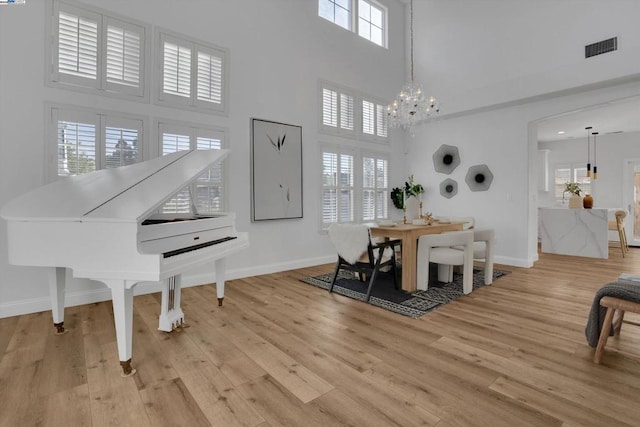 dining space with a high ceiling, a wealth of natural light, an inviting chandelier, and light hardwood / wood-style flooring