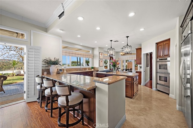 kitchen with hanging light fixtures, kitchen peninsula, a breakfast bar, stainless steel appliances, and light stone counters