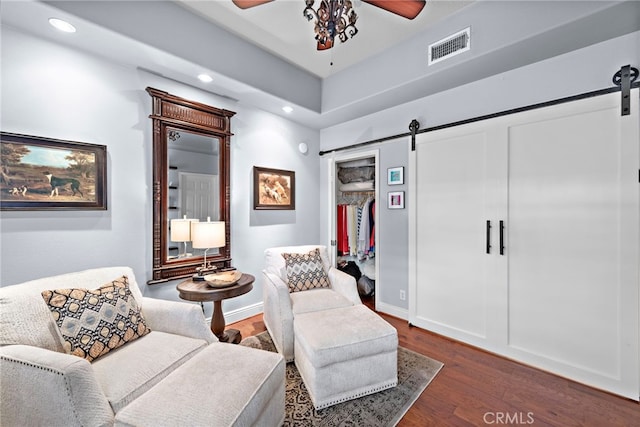 sitting room with ceiling fan, dark wood-type flooring, and a barn door