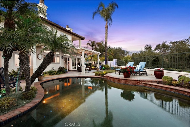 pool at dusk with a patio area and a pergola