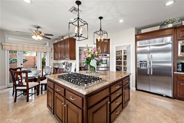 kitchen featuring pendant lighting, dark brown cabinetry, a kitchen island, built in appliances, and light stone counters