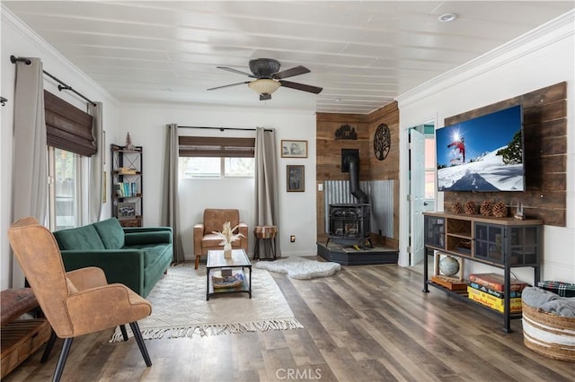 living room featuring a wood stove, wood-type flooring, crown molding, and a healthy amount of sunlight