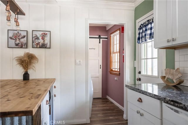 kitchen featuring a barn door, dark hardwood / wood-style flooring, dark stone countertops, ornamental molding, and white cabinets