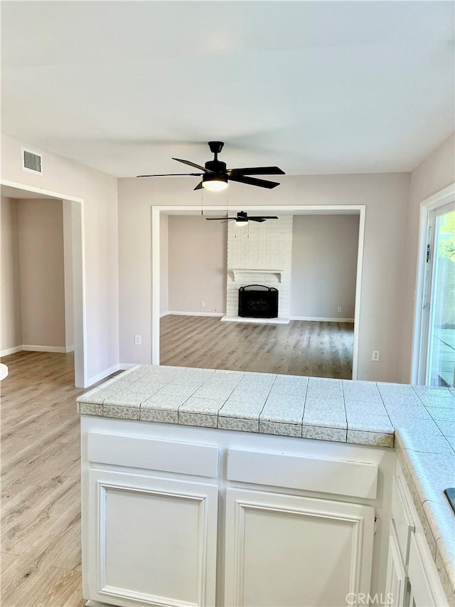 kitchen with a brick fireplace, white cabinets, ceiling fan, and light hardwood / wood-style flooring