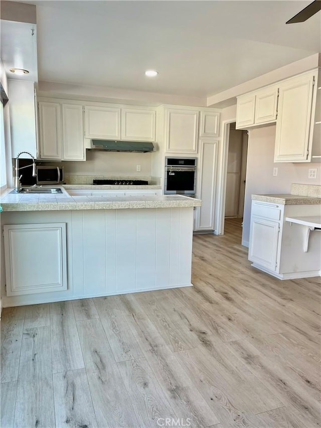 kitchen with sink, stainless steel oven, white cabinets, and light hardwood / wood-style floors