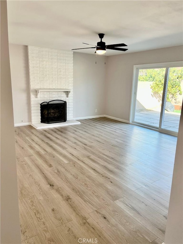 unfurnished living room featuring ceiling fan, a brick fireplace, and light wood-type flooring