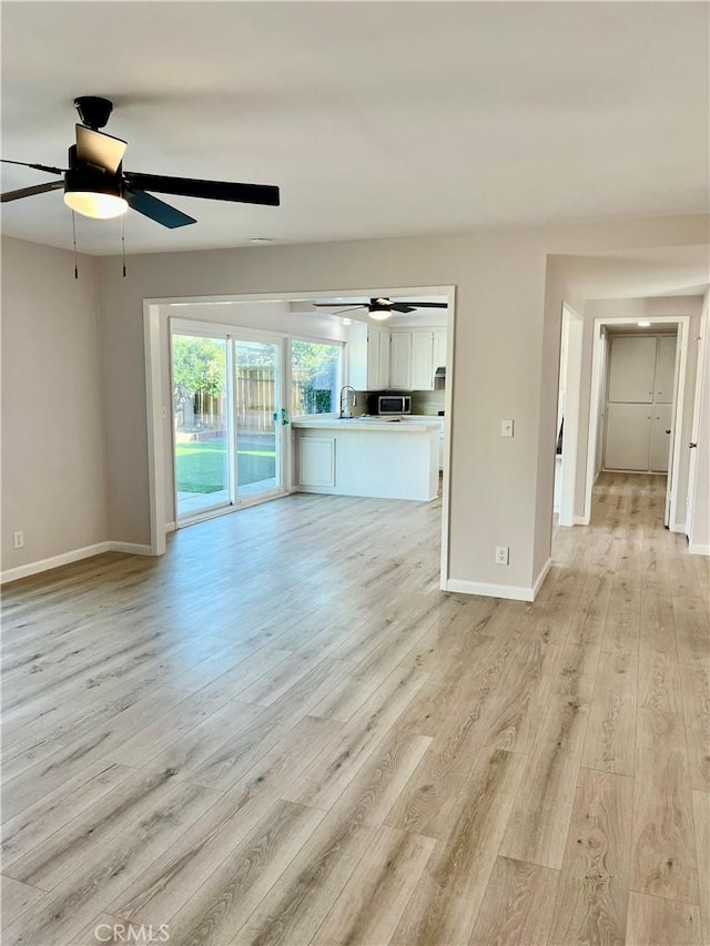 unfurnished living room featuring sink, light hardwood / wood-style flooring, and ceiling fan