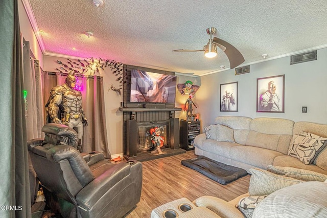 living room with ceiling fan, a fireplace, wood-type flooring, a textured ceiling, and ornamental molding