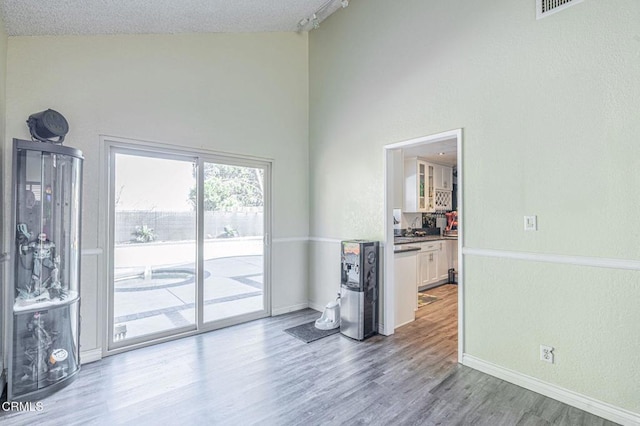 unfurnished room with high vaulted ceiling, a textured ceiling, baseboards, and wood finished floors