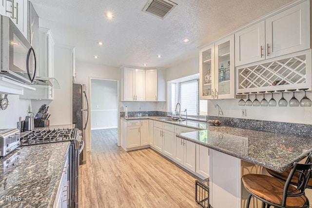 kitchen with stainless steel appliances, visible vents, white cabinets, a sink, and dark stone counters