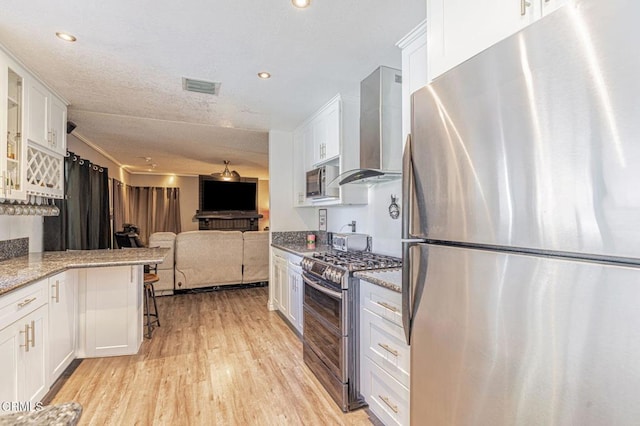 kitchen with stainless steel appliances, white cabinetry, open floor plan, wall chimney range hood, and glass insert cabinets