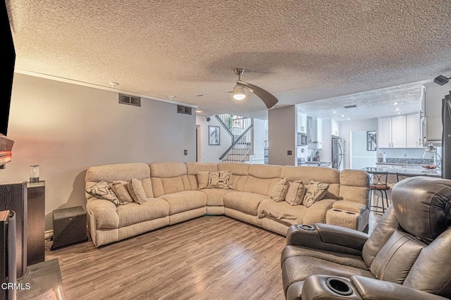 living room with visible vents, a ceiling fan, stairs, a textured ceiling, and light wood-style floors