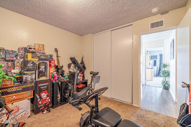 workout area with carpet, visible vents, a textured ceiling, and a textured wall