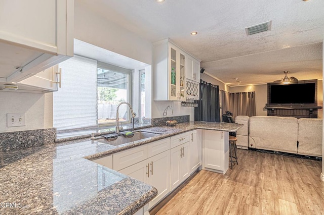 kitchen with white cabinetry, glass insert cabinets, a sink, and stone countertops