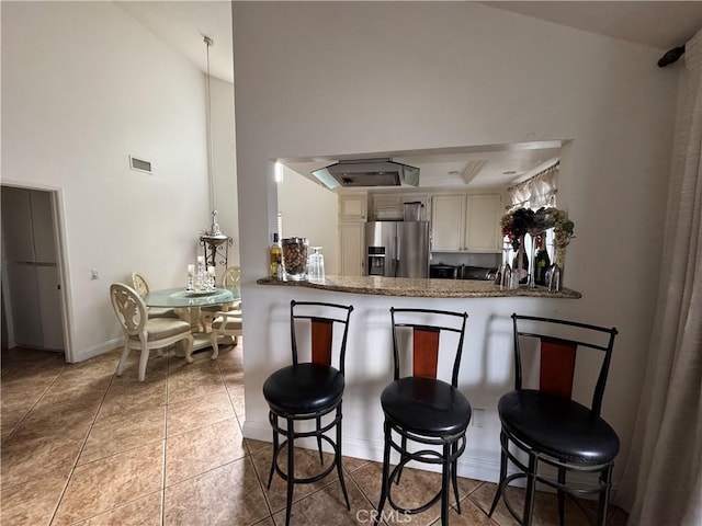 kitchen with stainless steel fridge with ice dispenser, kitchen peninsula, high vaulted ceiling, light tile patterned floors, and a breakfast bar area