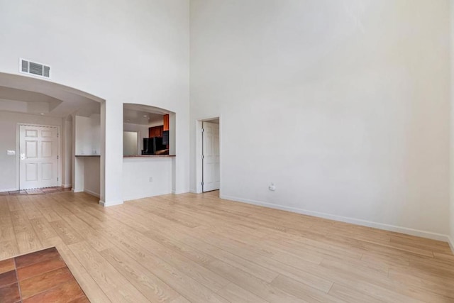 unfurnished living room with light wood-type flooring and a high ceiling