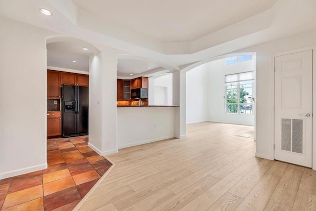 kitchen with black appliances, a raised ceiling, and light hardwood / wood-style flooring