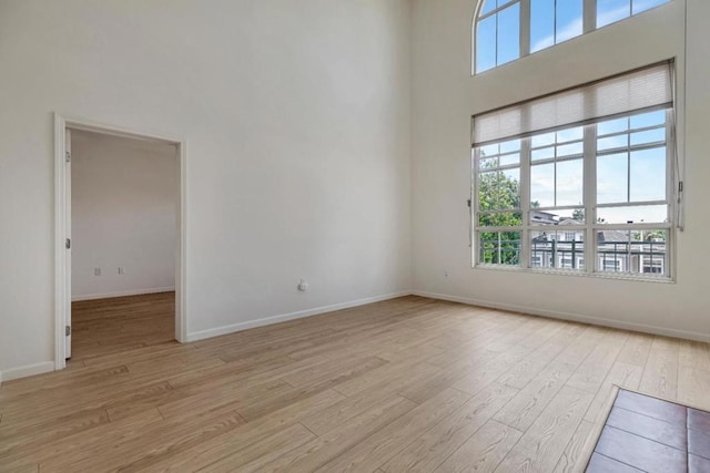 spare room featuring light hardwood / wood-style floors and a towering ceiling