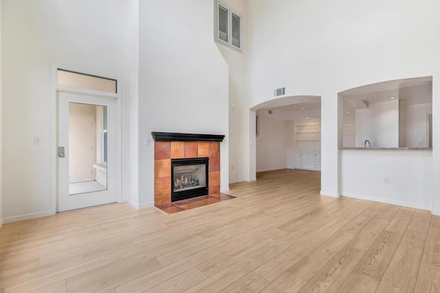 unfurnished living room featuring a fireplace, light hardwood / wood-style floors, and a towering ceiling