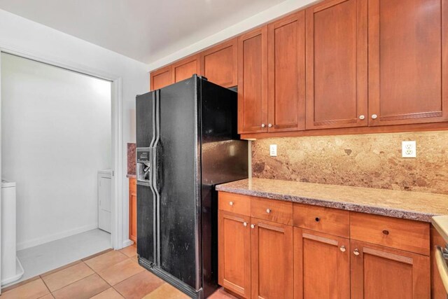 kitchen with light tile patterned floors, decorative backsplash, black refrigerator with ice dispenser, and light stone countertops