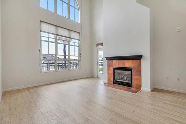 unfurnished living room featuring a high ceiling, light hardwood / wood-style flooring, and a tiled fireplace