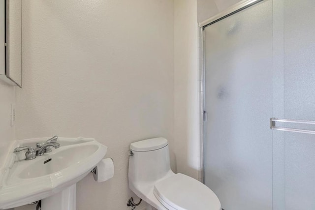 bathroom with a shower with shower door, sink, and toilet