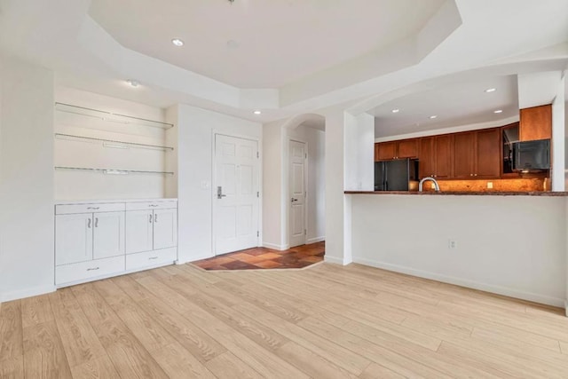 unfurnished living room with sink, a tray ceiling, and light wood-type flooring