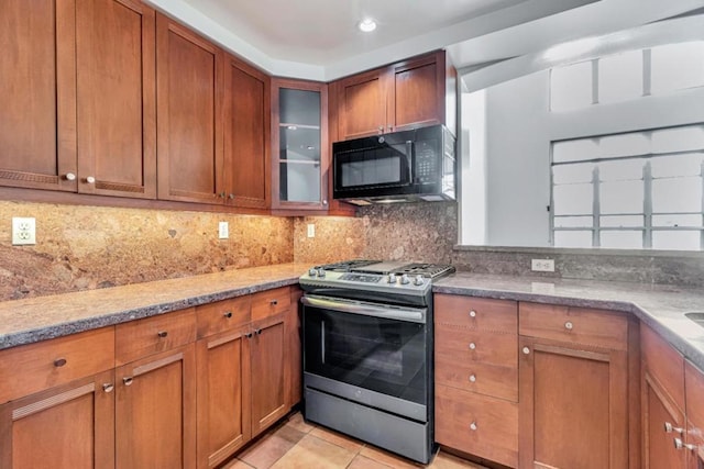 kitchen featuring light stone counters, backsplash, light tile patterned floors, and stainless steel gas range oven