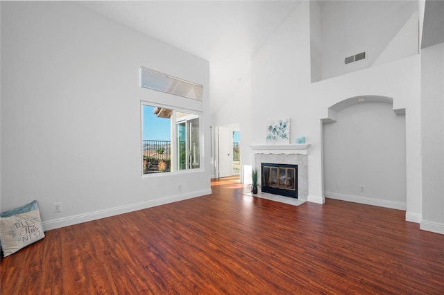 unfurnished living room featuring dark wood-type flooring, a premium fireplace, and a towering ceiling