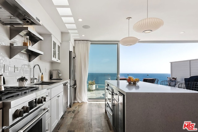 kitchen featuring decorative light fixtures, white cabinetry, dark hardwood / wood-style flooring, sink, and a water view