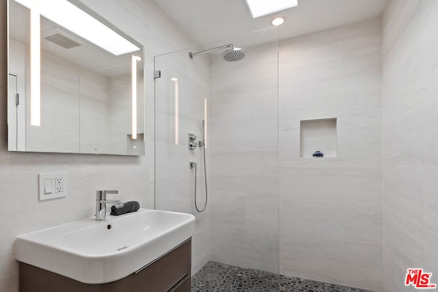 bathroom featuring a tile shower, vanity, and tile walls