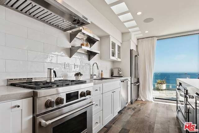 kitchen with appliances with stainless steel finishes, a water view, white cabinets, and wall chimney range hood