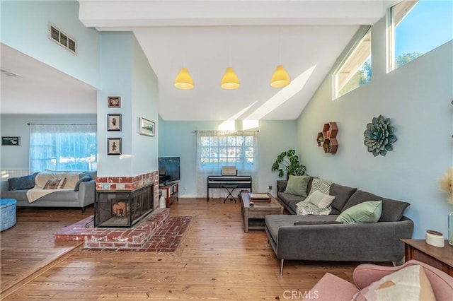 living area with a wealth of natural light, visible vents, beam ceiling, and wood finished floors