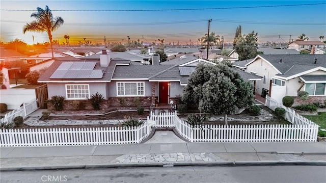 view of front of property featuring a fenced front yard, a residential view, and roof mounted solar panels