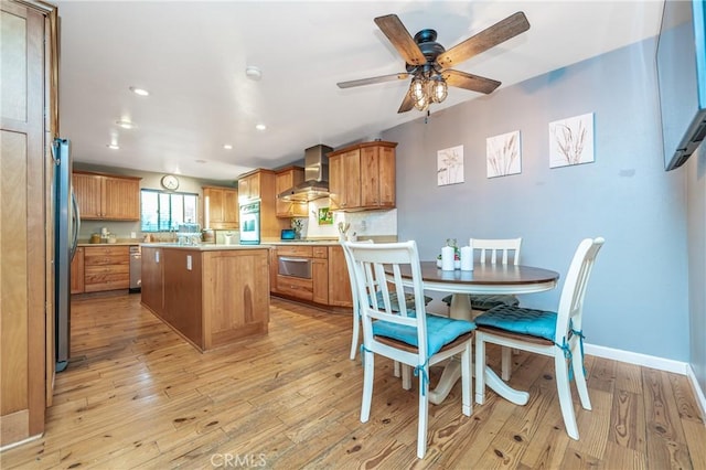 kitchen featuring light countertops, wall chimney range hood, appliances with stainless steel finishes, and light wood-style floors