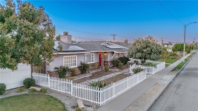 view of front facade with a fenced front yard, stucco siding, and solar panels