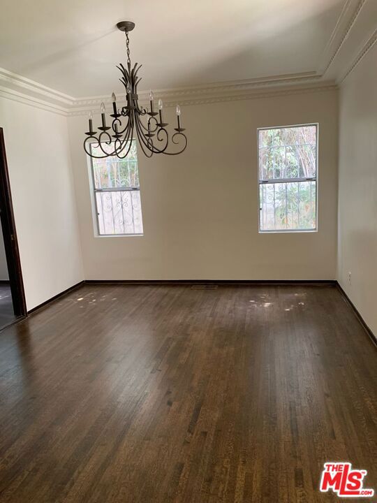 unfurnished dining area with an inviting chandelier, a wealth of natural light, crown molding, and dark hardwood / wood-style floors