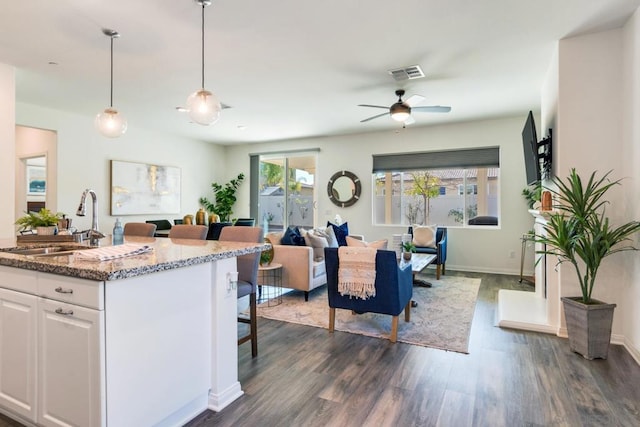 kitchen featuring pendant lighting, sink, dark stone countertops, white cabinets, and a kitchen breakfast bar