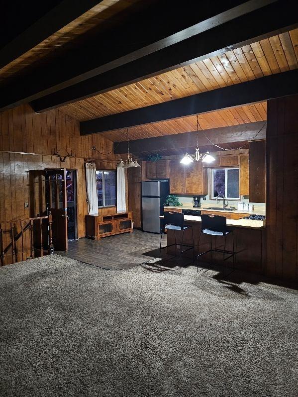 interior space with pendant lighting, wooden walls, sink, a breakfast bar area, and stainless steel fridge