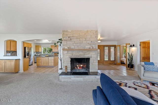 carpeted living room with crown molding, a stone fireplace, and a healthy amount of sunlight