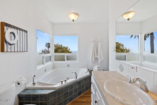 bathroom with hardwood / wood-style flooring, a relaxing tiled tub, toilet, and vanity