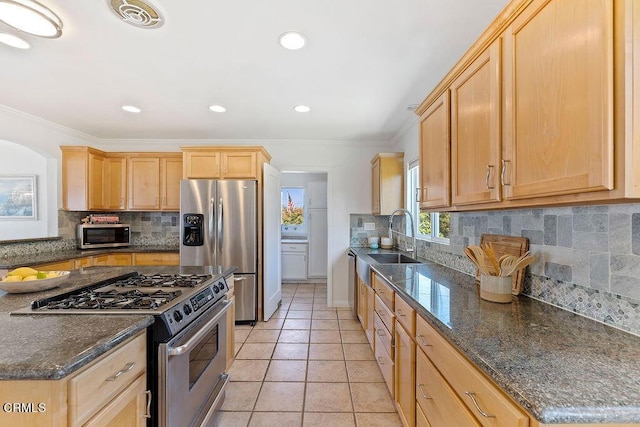 kitchen with light tile patterned floors, stainless steel appliances, dark stone countertops, crown molding, and sink