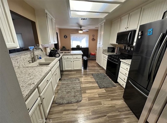 kitchen with kitchen peninsula, sink, stainless steel refrigerator, white cabinetry, and black gas range oven