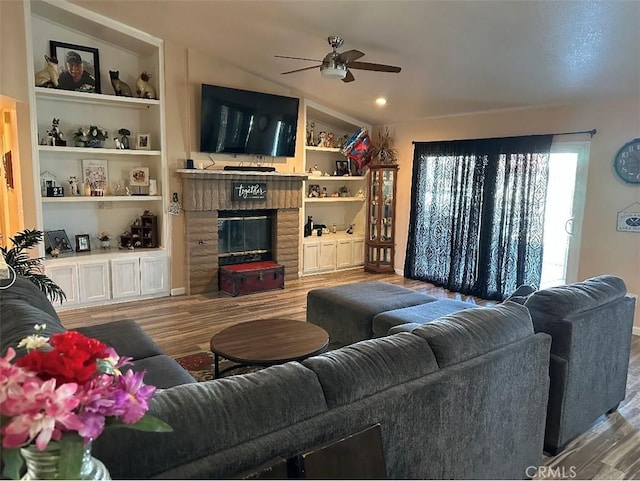 living room featuring hardwood / wood-style floors, a brick fireplace, ceiling fan, lofted ceiling, and built in features