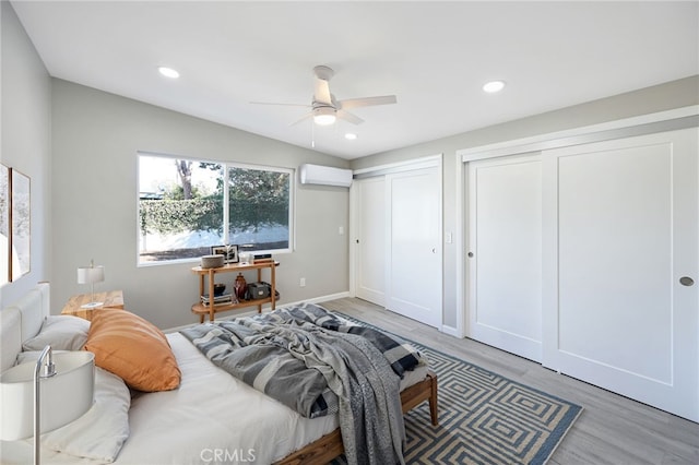 bedroom featuring two closets, wood-type flooring, a wall mounted AC, vaulted ceiling, and ceiling fan